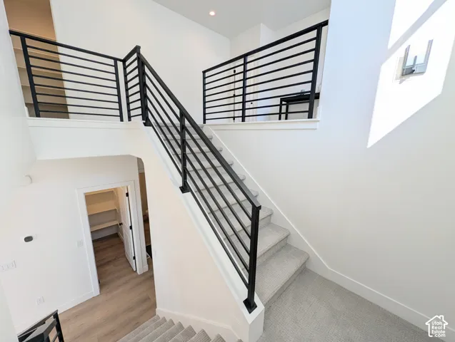 Multi-level interior featuring modern horizontal black railings, light gray carpeted stairs, recessed lighting, and wood-finish flooring