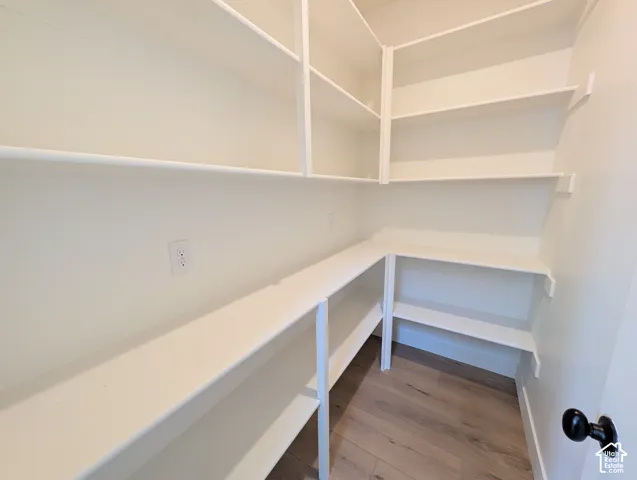 Walk-in pantry featuring extensive white shelving, wood-finish flooring, and an electrical outlet