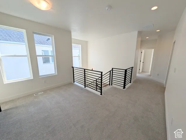 Upper-level landing featuring textured carpet, multiple windows, a modern black metal railing, and recessed ceiling lighting