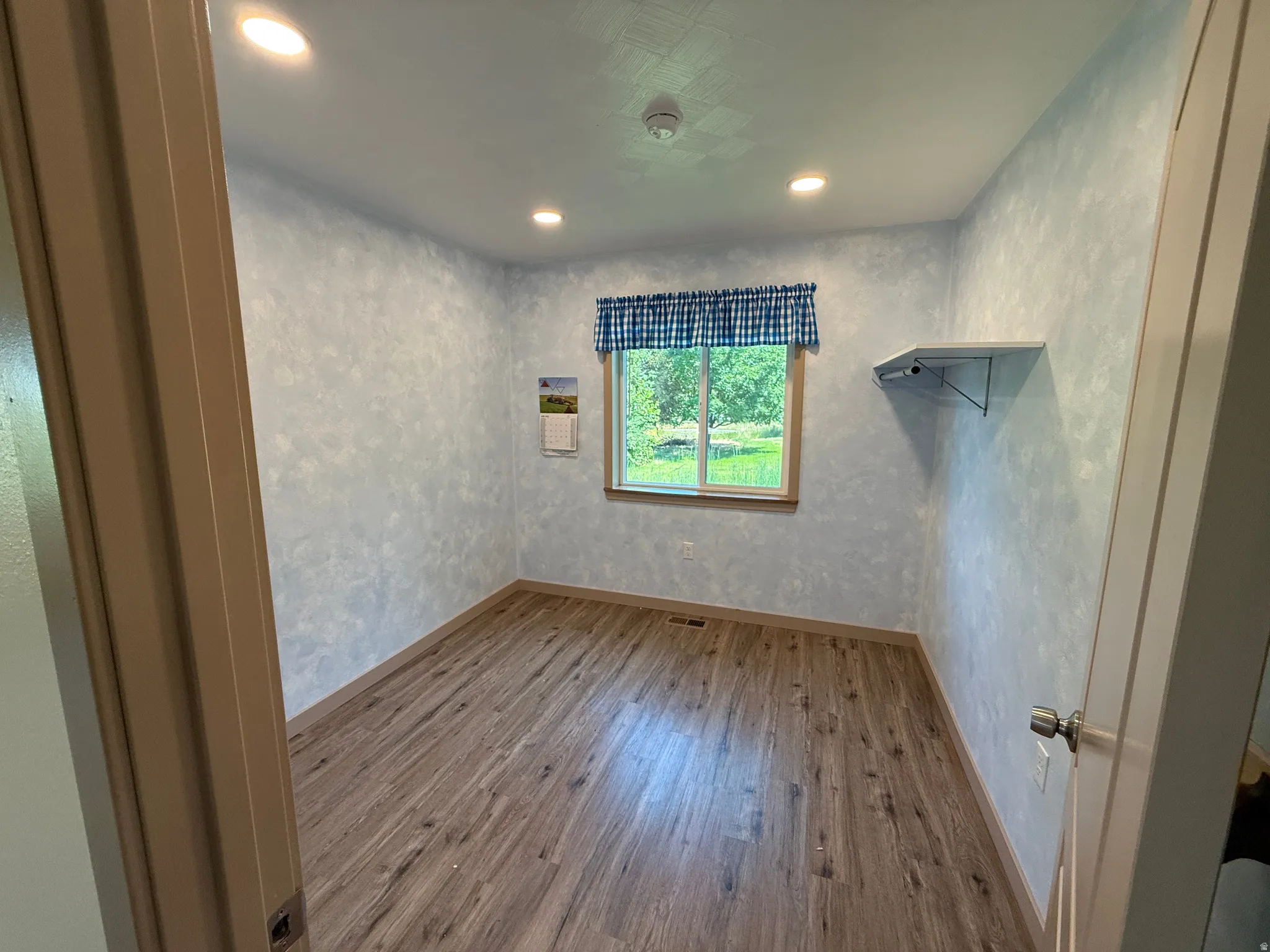 Interior room featuring wood-finish flooring, recessed ceiling lighting, a window with natural light, a built-in wall shelf, and light-toned walls