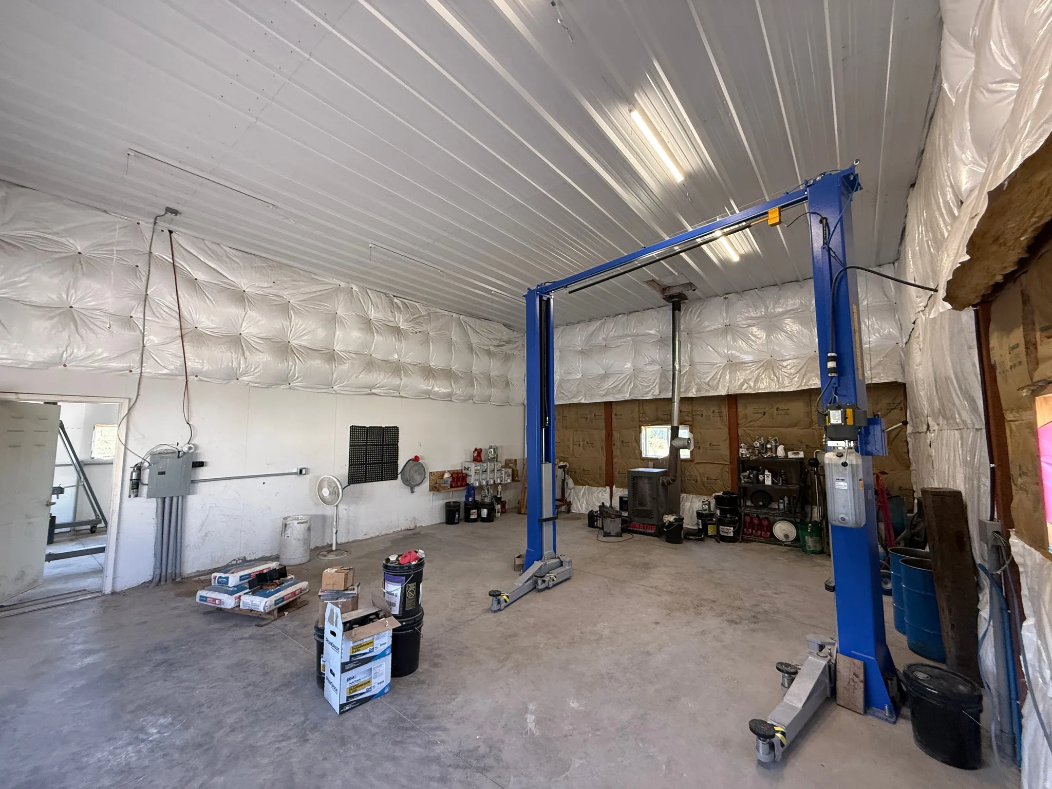 Spacious workshop featuring a two-post vehicle lift, concrete flooring, and high corrugated metal ceilings