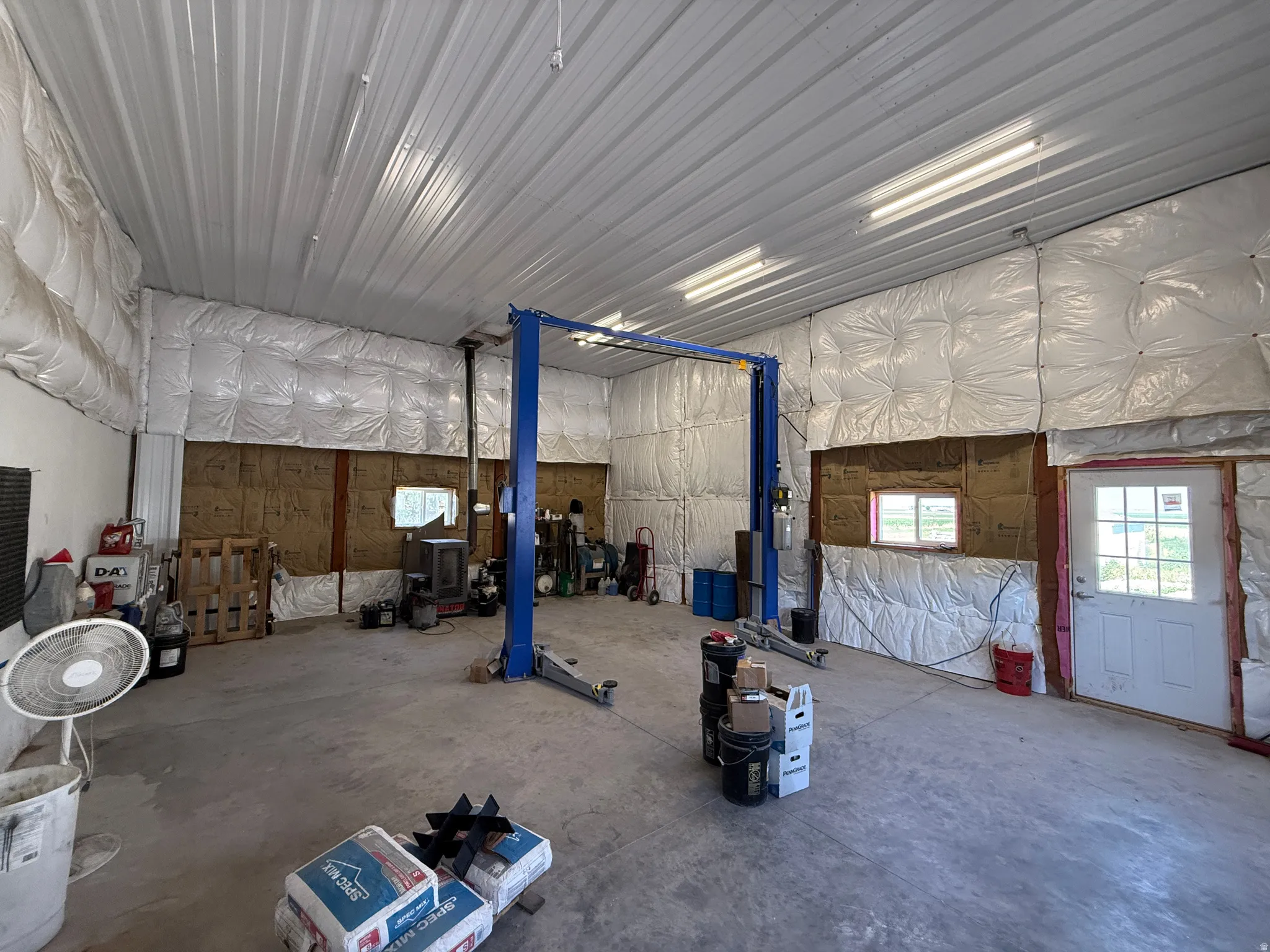 Spacious garage interior featuring a high corrugated metal ceiling, concrete flooring, and exposed insulation
