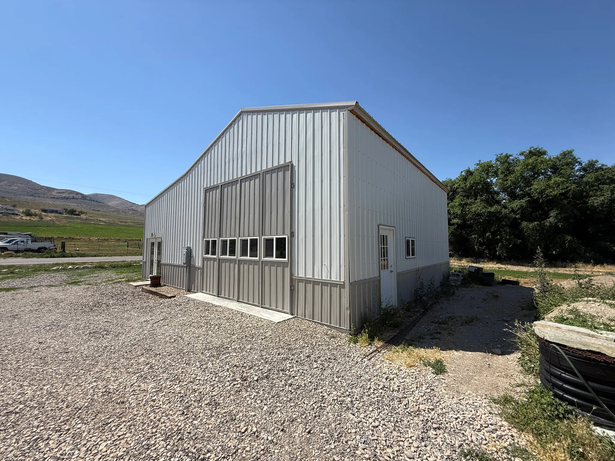 Metal-sided barn featuring a large main entrance with multiple windows, an additional entry door, and a gravel parking area