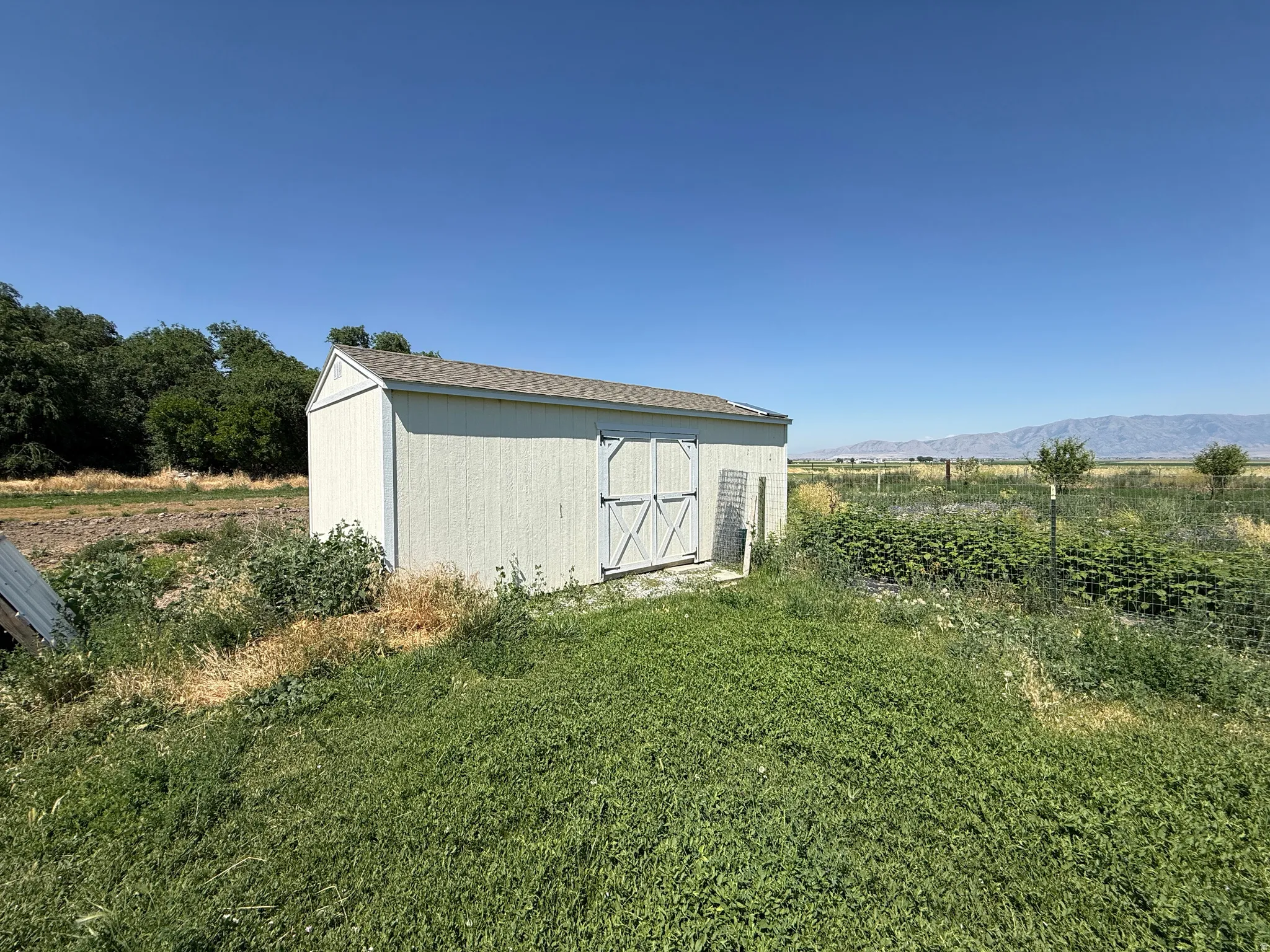 White-sided storage shed featuring double doors and a shingled roof