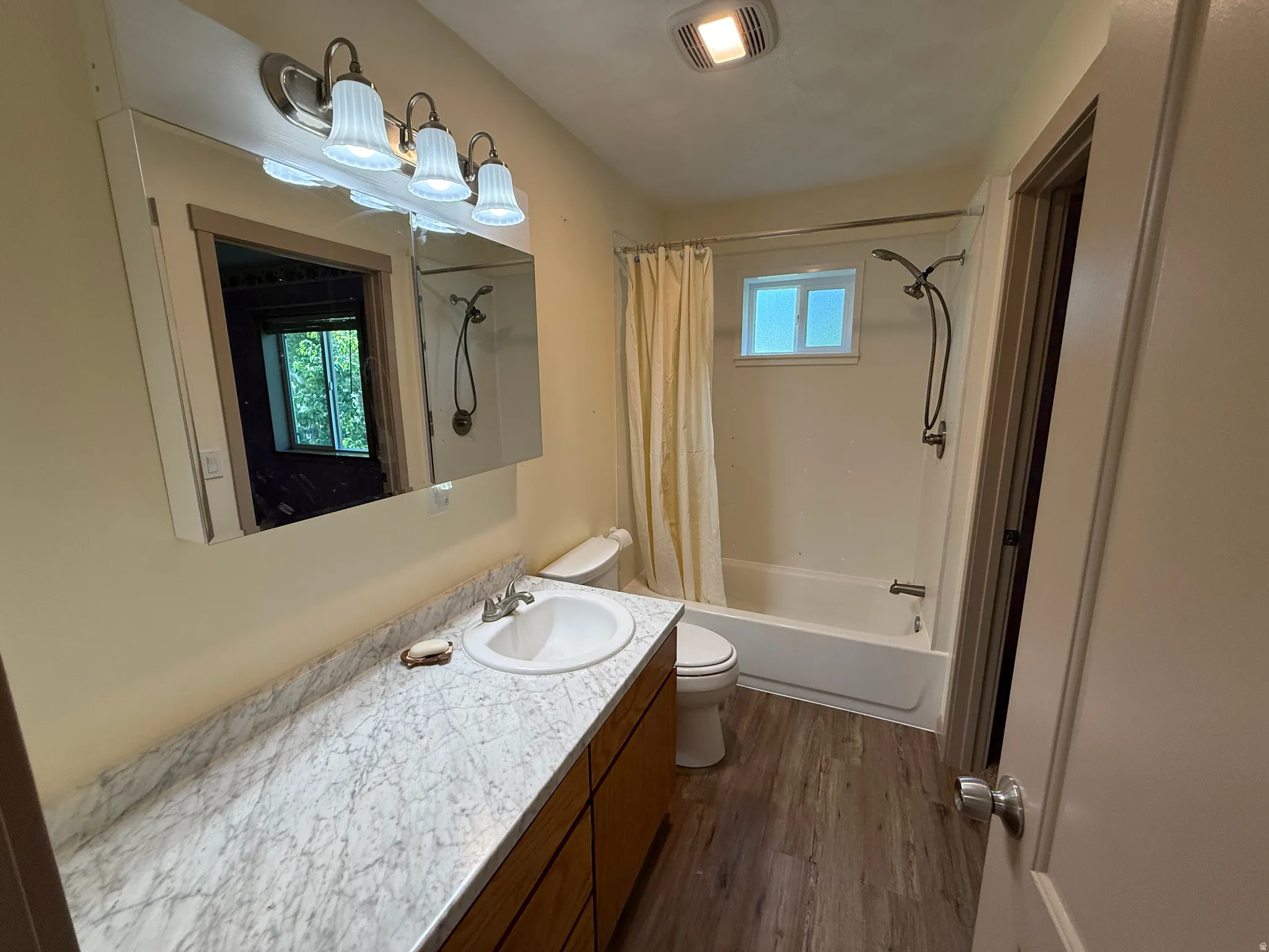 Bathroom featuring a single vanity with a white countertop and wood-finish cabinetry, a toilet, a bathtub with an overhead shower, and wood-finish flooring
