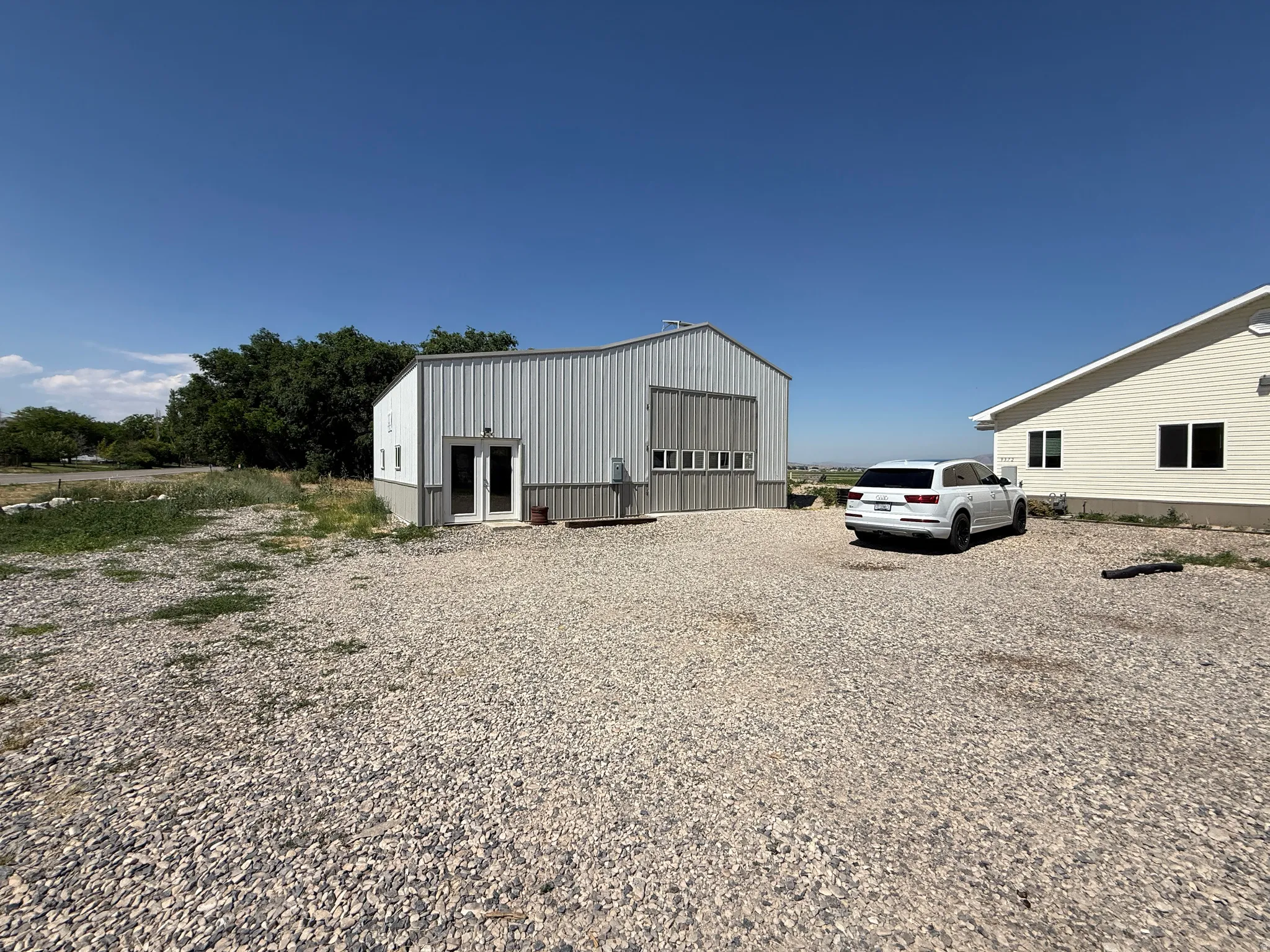 Gravel parking area featuring a metal-sided outbuilding with multiple windows and a double door entrance