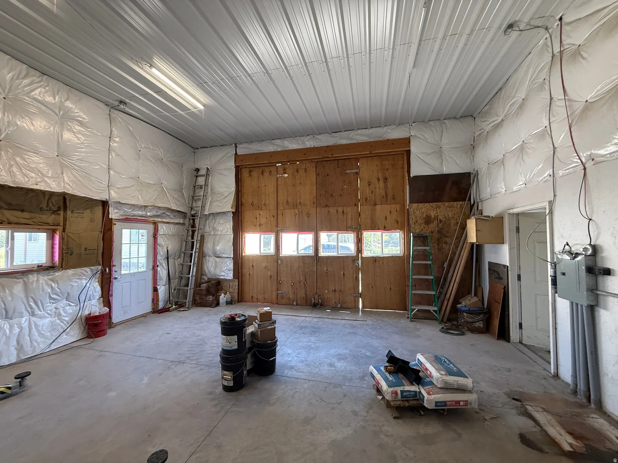 Spacious utility building featuring a concrete floor, high metal ceiling, large wooden double doors with integrated windows, and an insulated wall structure