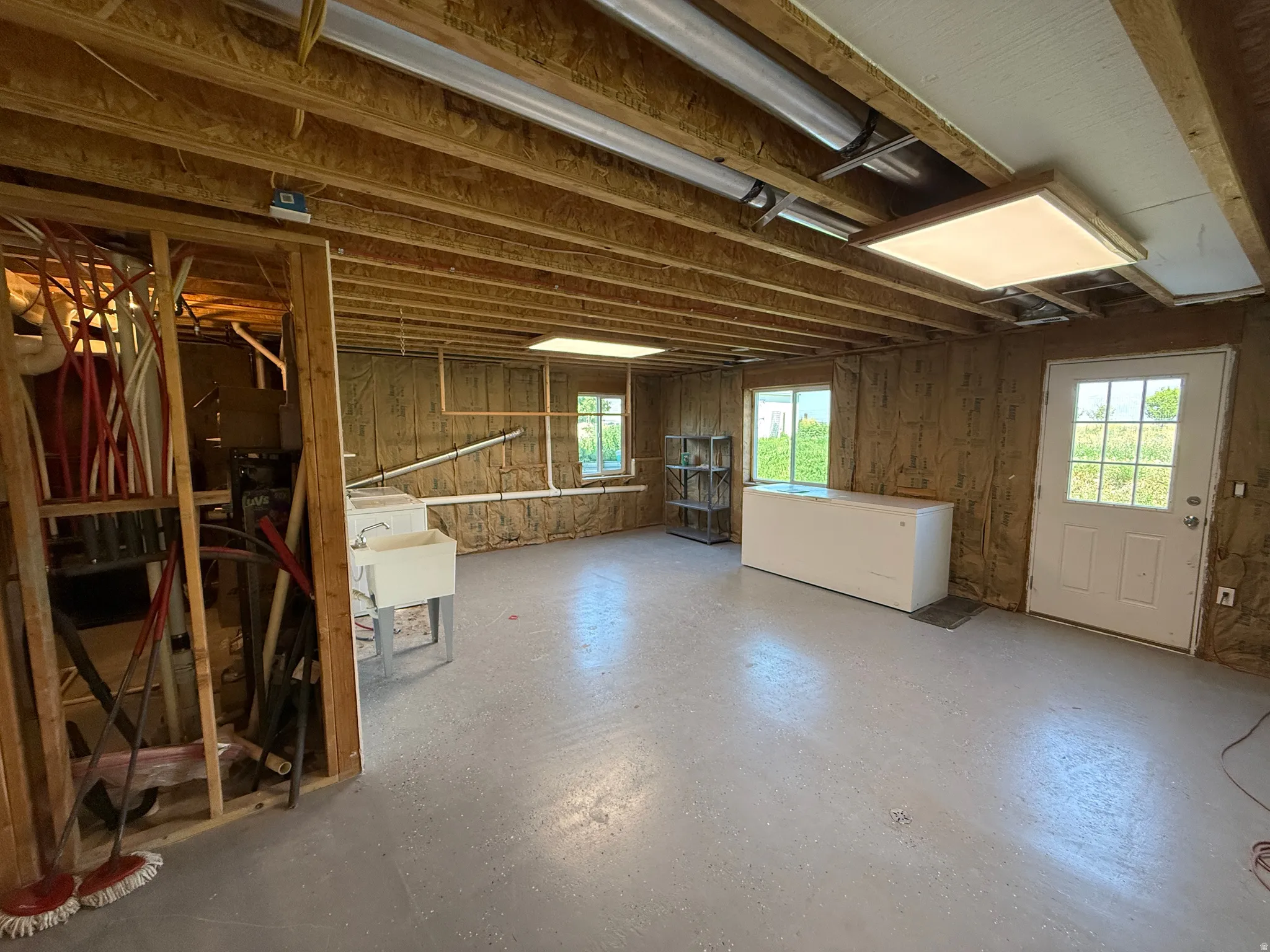 Expansive utility space featuring a light gray finished concrete floor, exposed wood ceiling joists, and visible insulation along the walls