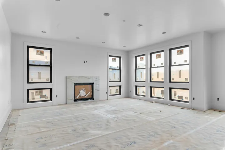 Recessed lighting, large windows, sleek black window frames, white wall finishes, and a fireplace with a light-toned surround