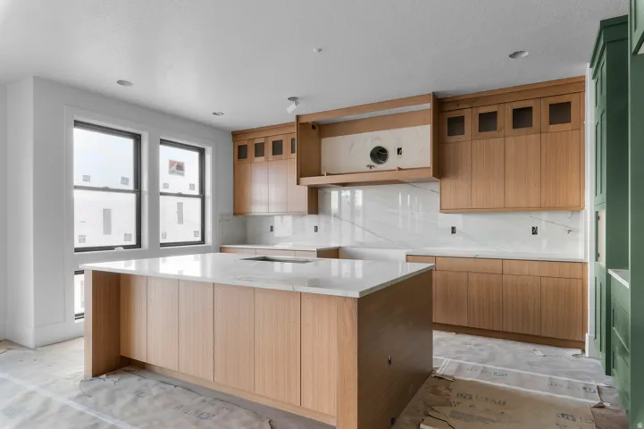 Kitchen featuring a central island with countertop, natural wood-finish cabinetry, white slab backsplash, and black-framed windows