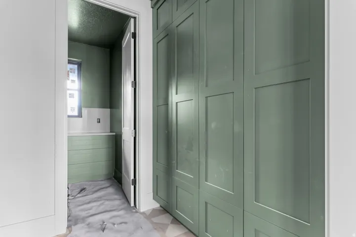 Floor-to-ceiling custom cabinetry with paneling, window with dark trim, light green wall finishes, and a built-in counter
