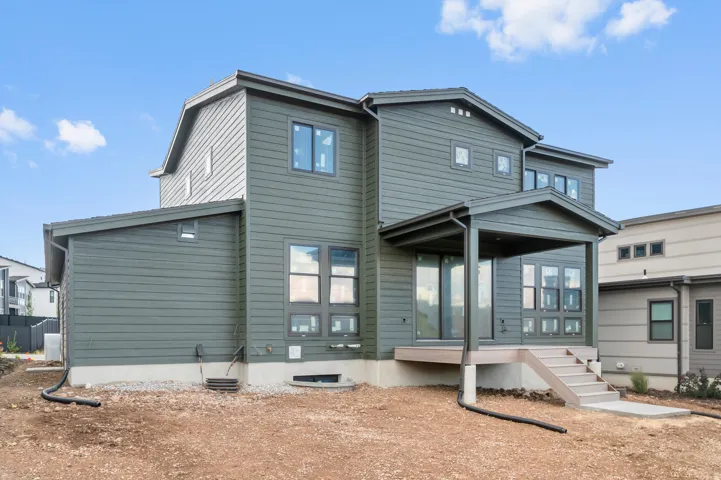 Modern exterior featuring dark siding, multiple window configurations, a covered patio, and a concrete patio with steps