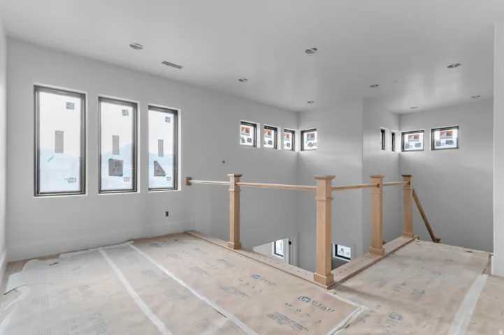 Spacious upper-level landing with multiple windows, recessed ceiling lighting, and a light wood railing