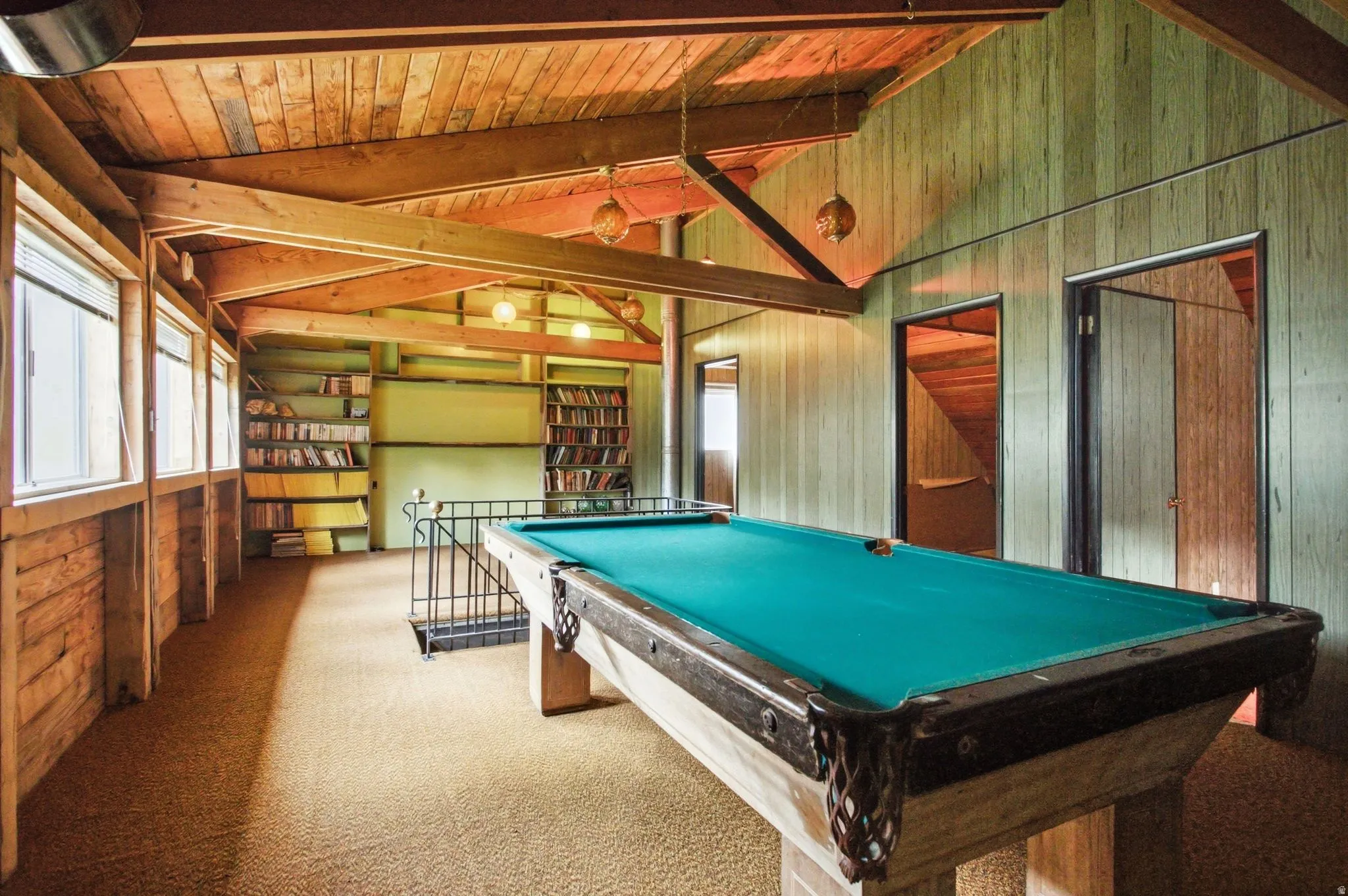 Recreation room featuring exposed wood beam ceiling, wood-paneled walls, built-in shelving, and multiple windows