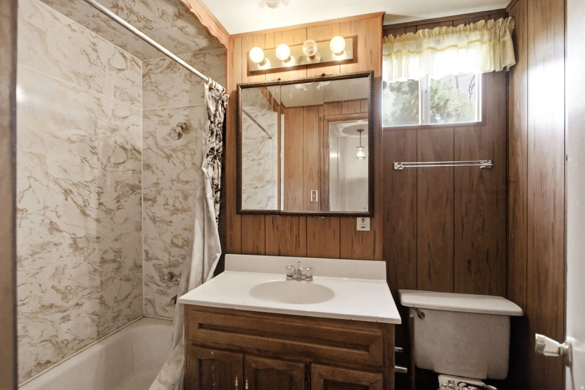 Bathroom featuring a white tub with a marbled-pattern surround, wood-paneled walls, a single-sink vanity, and a window