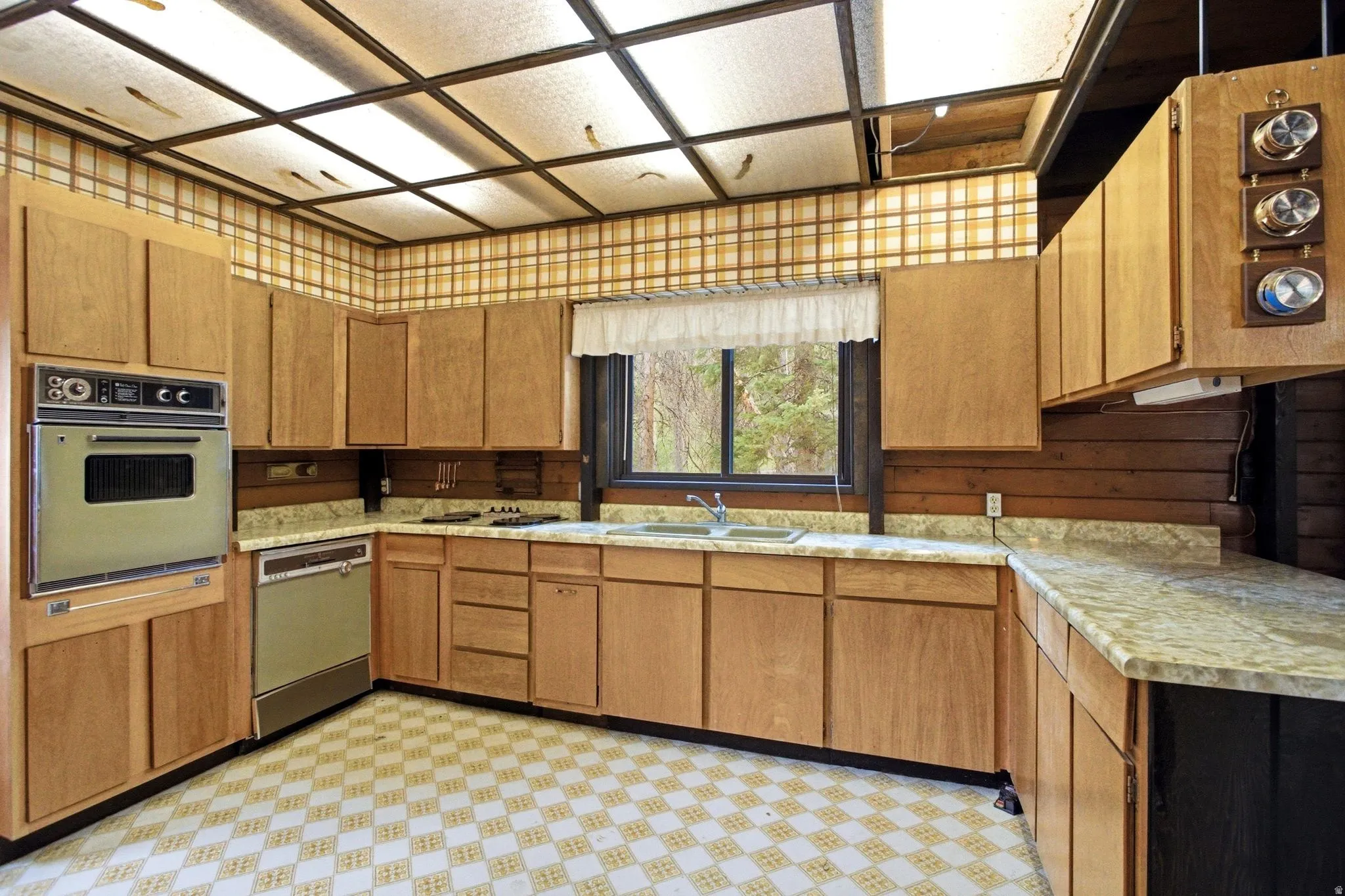 Kitchen featuring a built-in oven, dishwasher, double basin sink, ample wood-finish cabinetry, and a patterned tiled floor