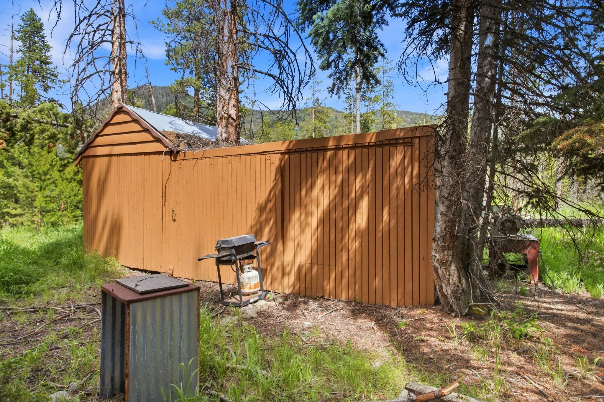 Detached shed structure featuring horizontal and vertical wood siding, a partial gable roof, and a metal roof section