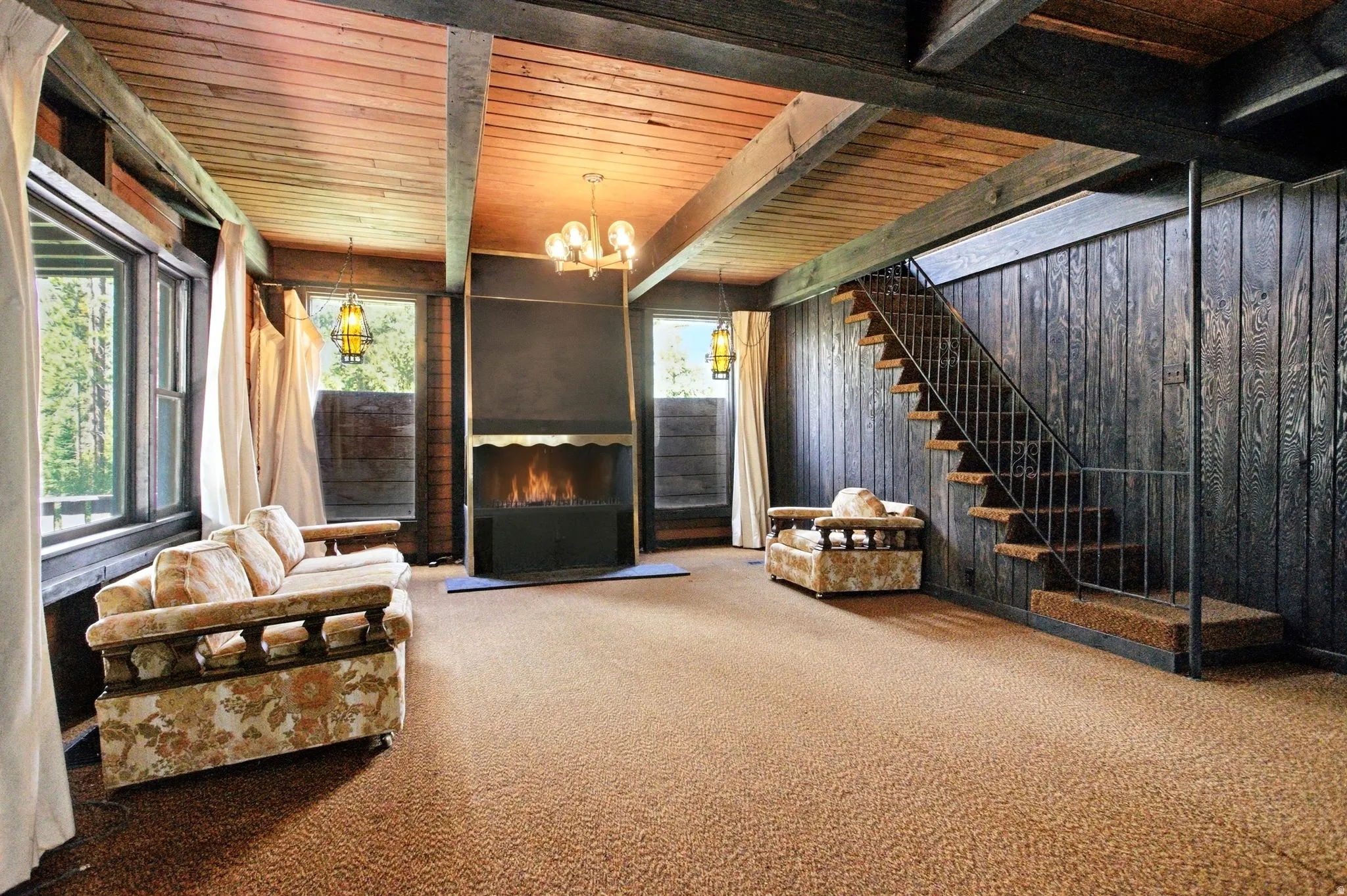 Spacious room featuring a wood-paneled ceiling with exposed beams, a built-in fireplace, and large windows