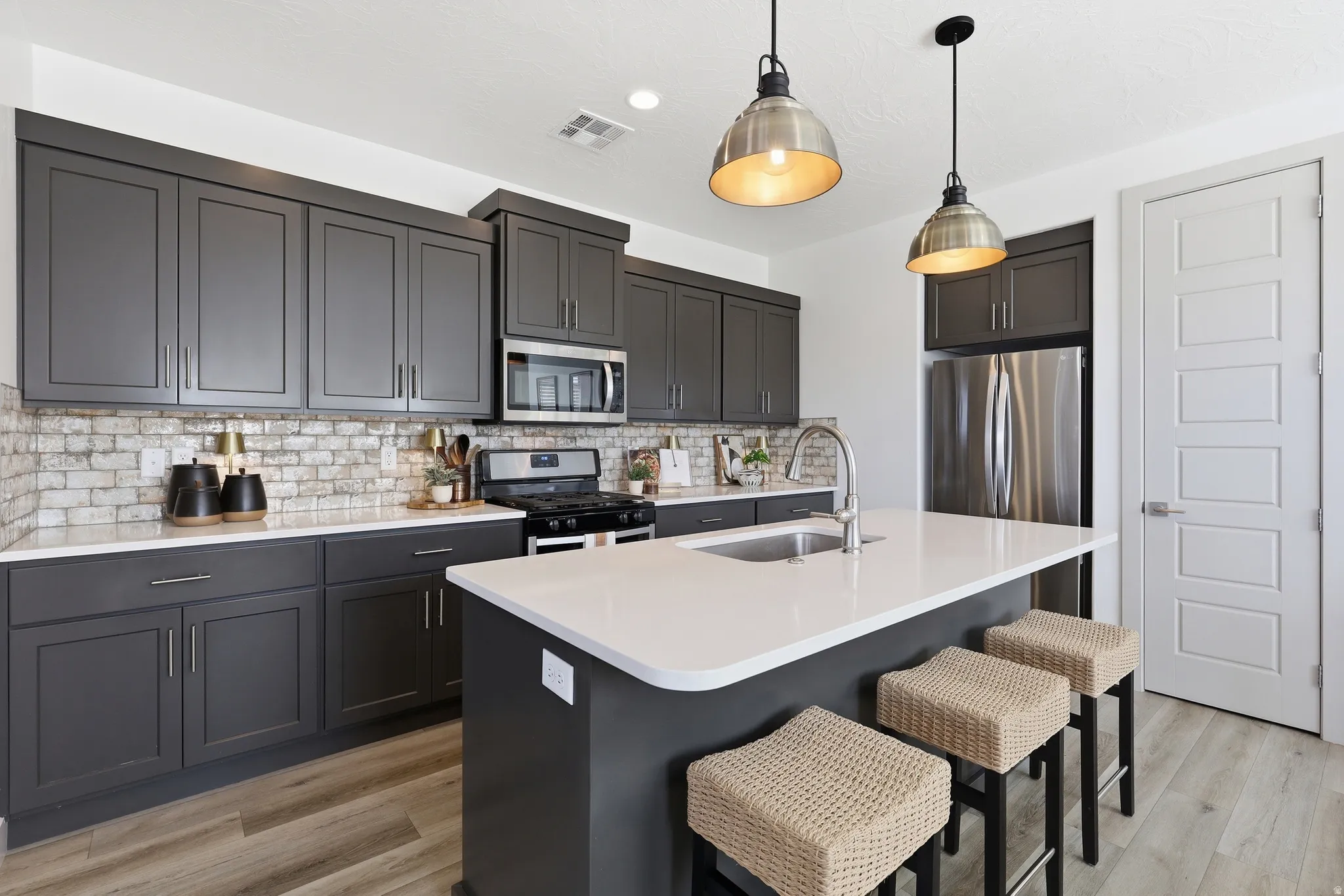Kitchen featuring dark gray cabinetry, stainless steel appliances, white countertops, and a subway tile backsplash