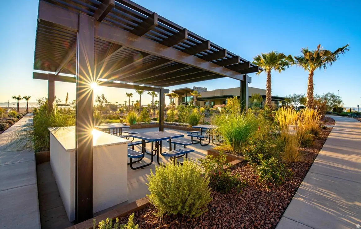 Outdoor covered patio featuring a built-in counter with a light-toned countertop, multiple picnic tables, and abundant landscaping with mature palm trees