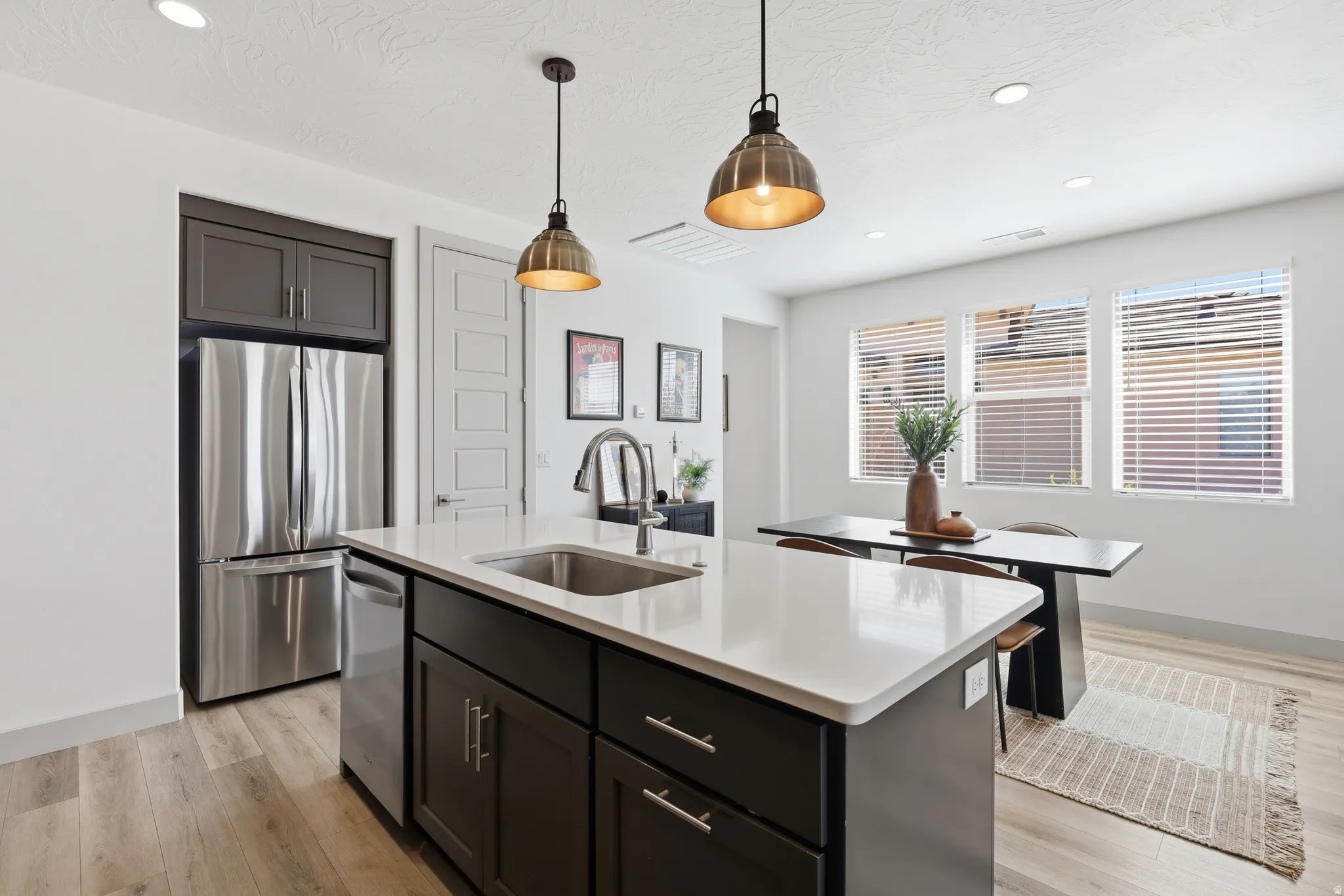 Kitchen island with a white countertop and dark cabinetry, featuring a stainless steel sink and integrated dishwasher
