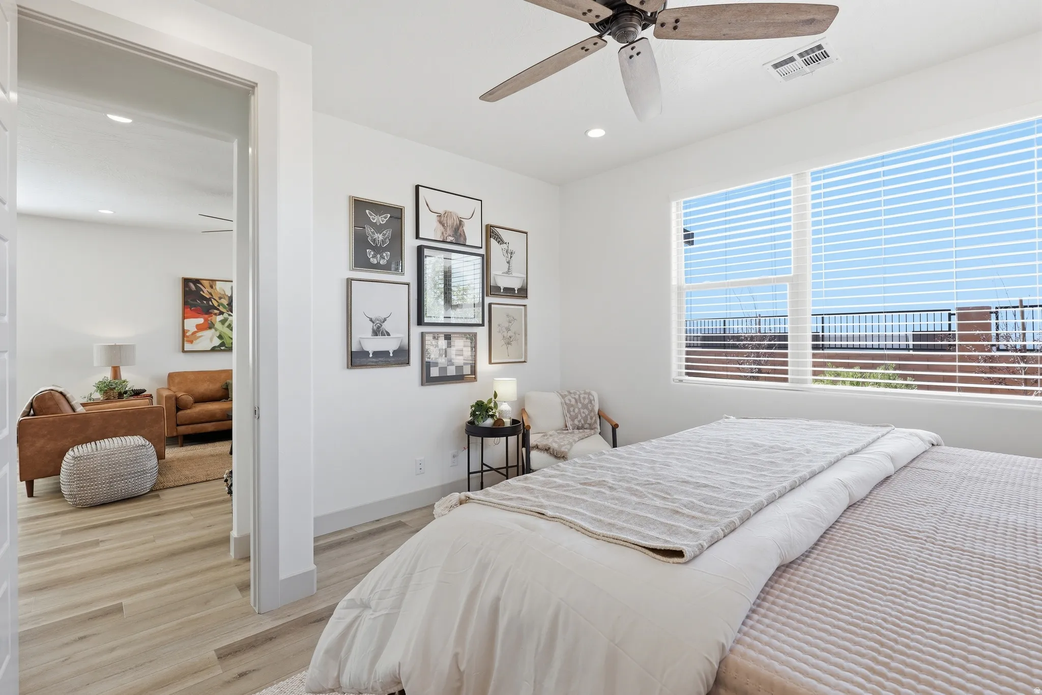Spacious bedroom with a large window featuring horizontal blinds, a ceiling fan, and wood-finish flooring