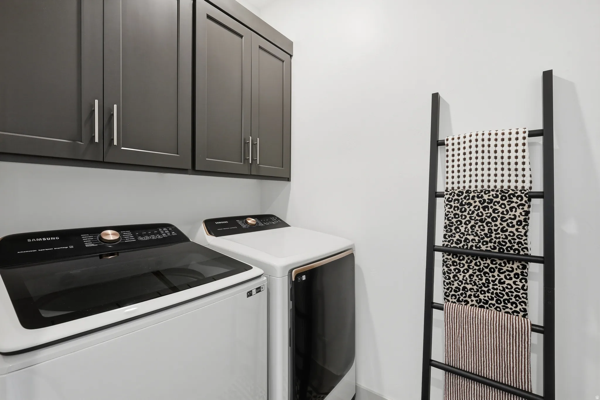 Laundry area featuring dark gray upper cabinetry with brushed nickel hardware, white walls, and a light gray baseboard