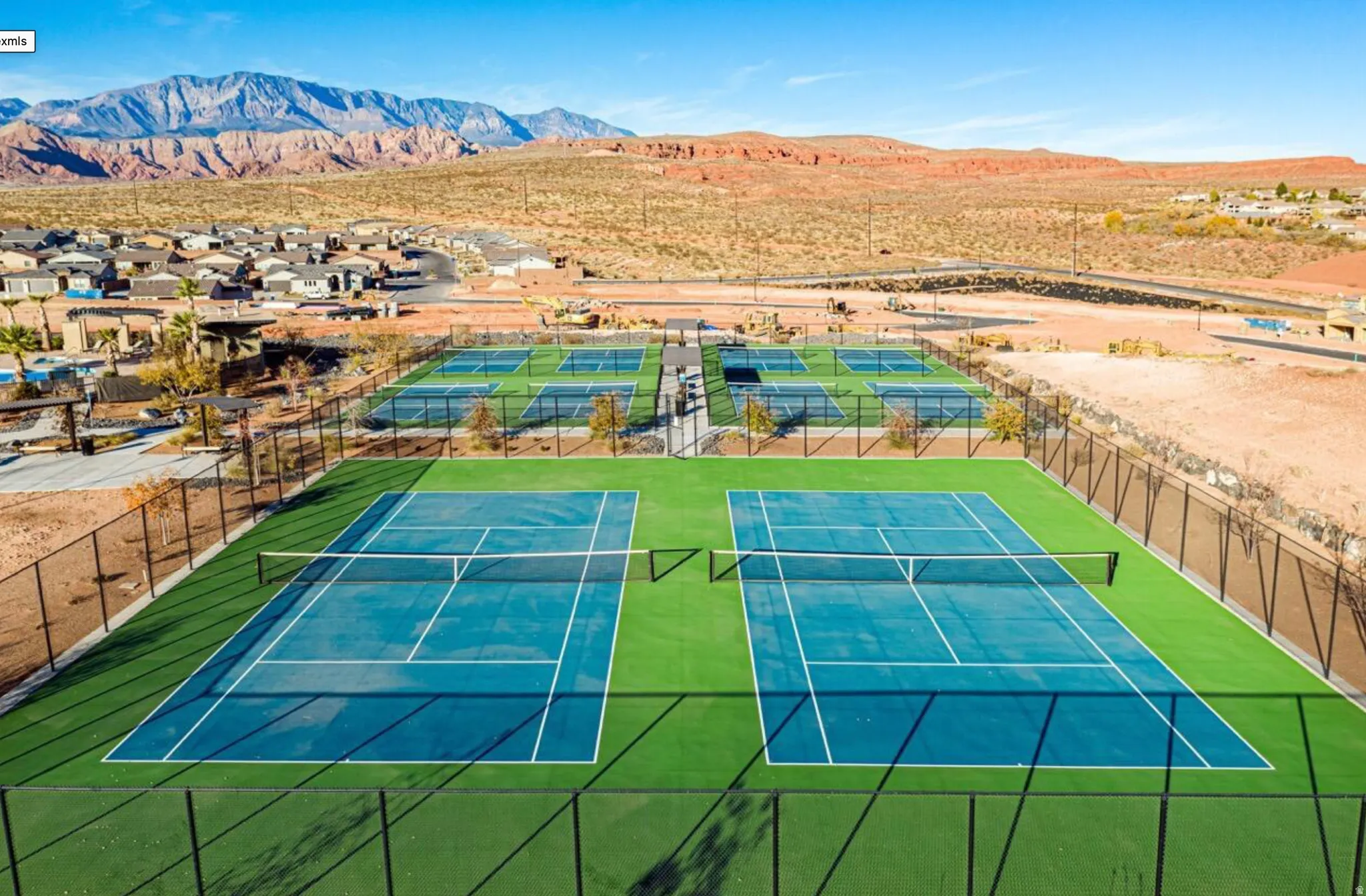 Multiple blue tennis courts with green surrounding turf