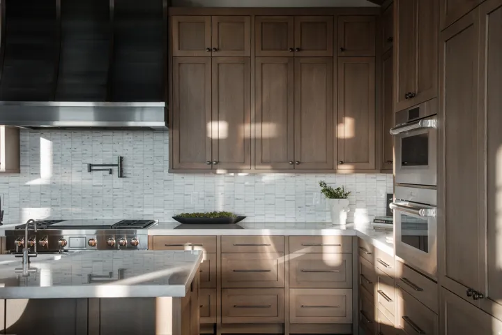 Gourmet kitchen featuring a professional-grade range, stainless steel appliances, custom wood cabinetry, stone countertops, and a full-height tile backsplash