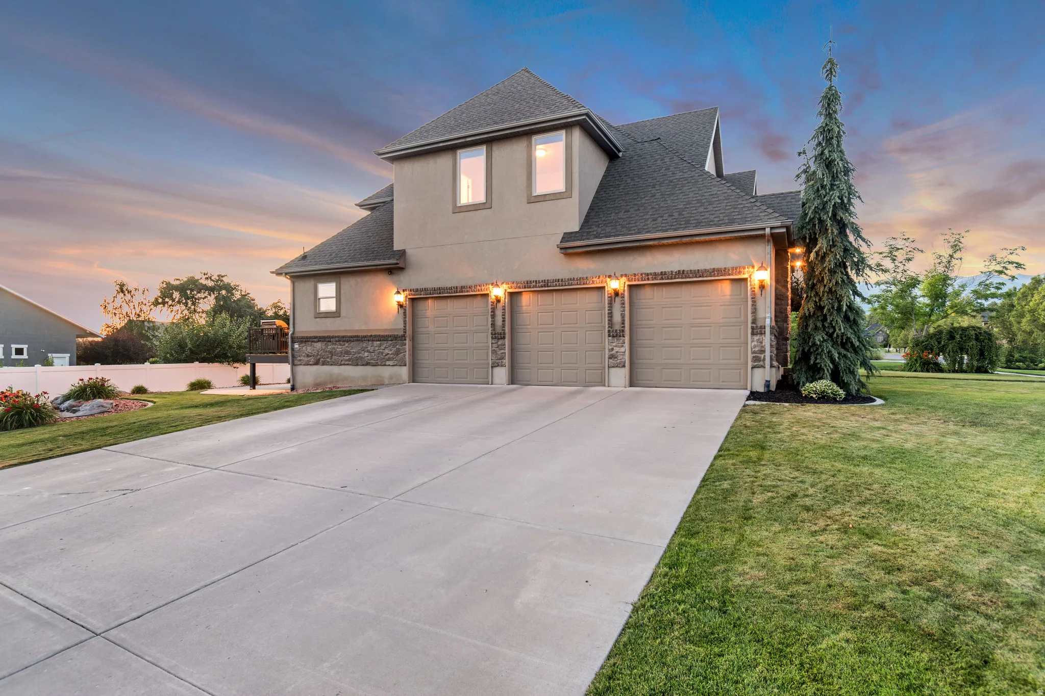 Stucco and stone facade home featuring a three-car garage with individual doors and exterior lighting