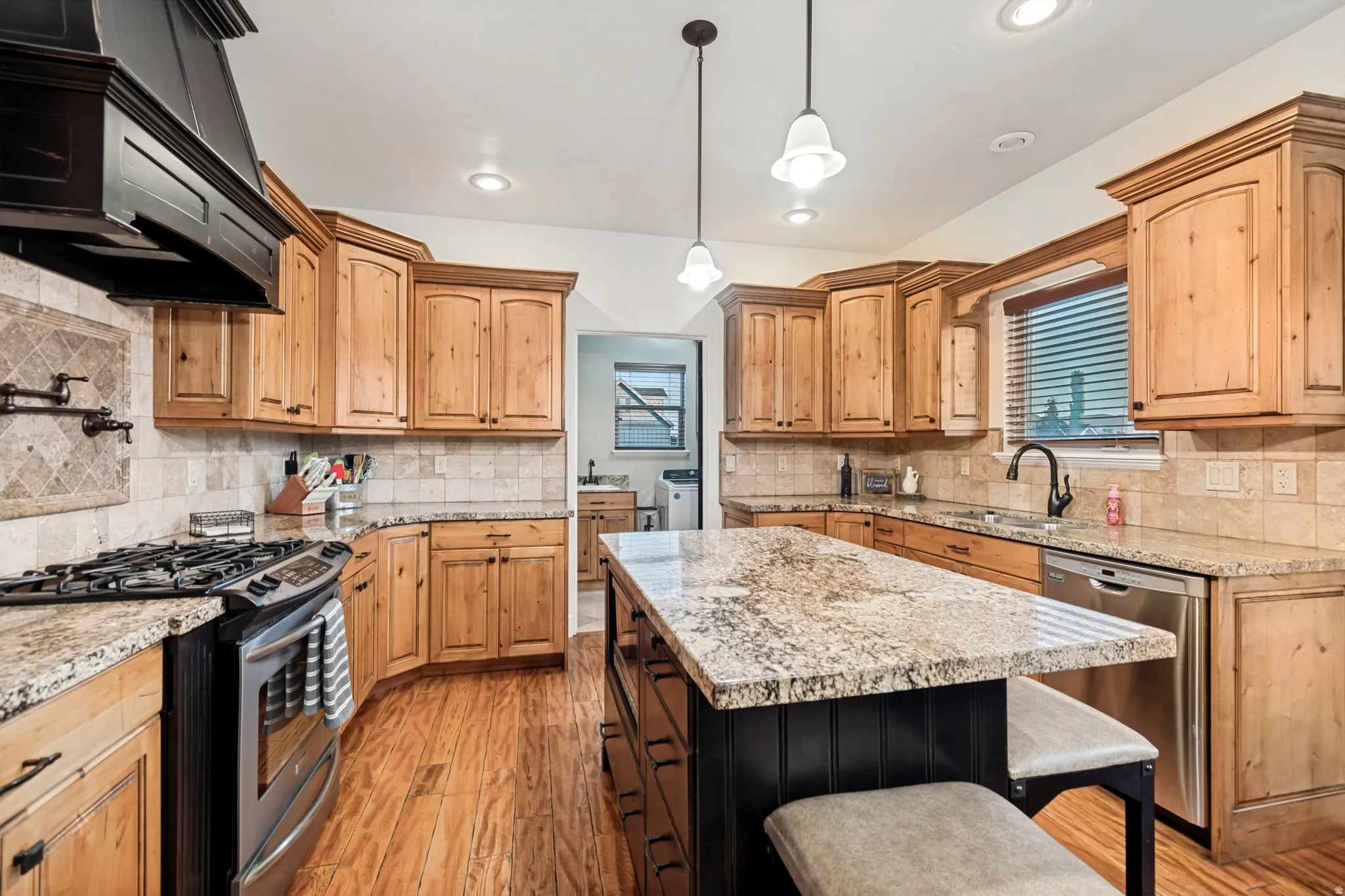 Gourmet kitchen featuring a central island with granite countertop, stainless steel appliances, hardwood flooring, and natural wood cabinetry.