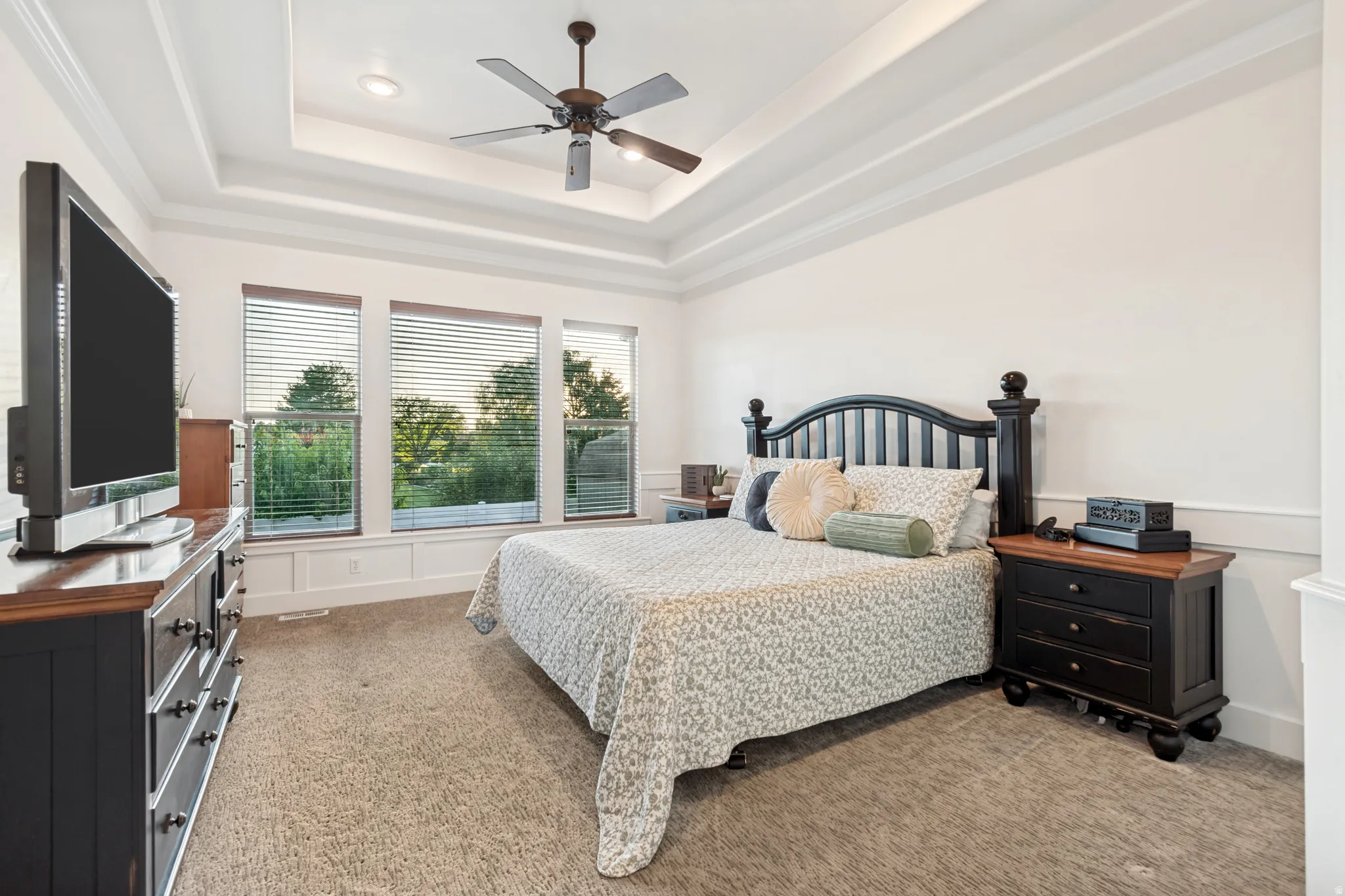Main floor primary suite bedroom with tray ceiling and ceiling fan.