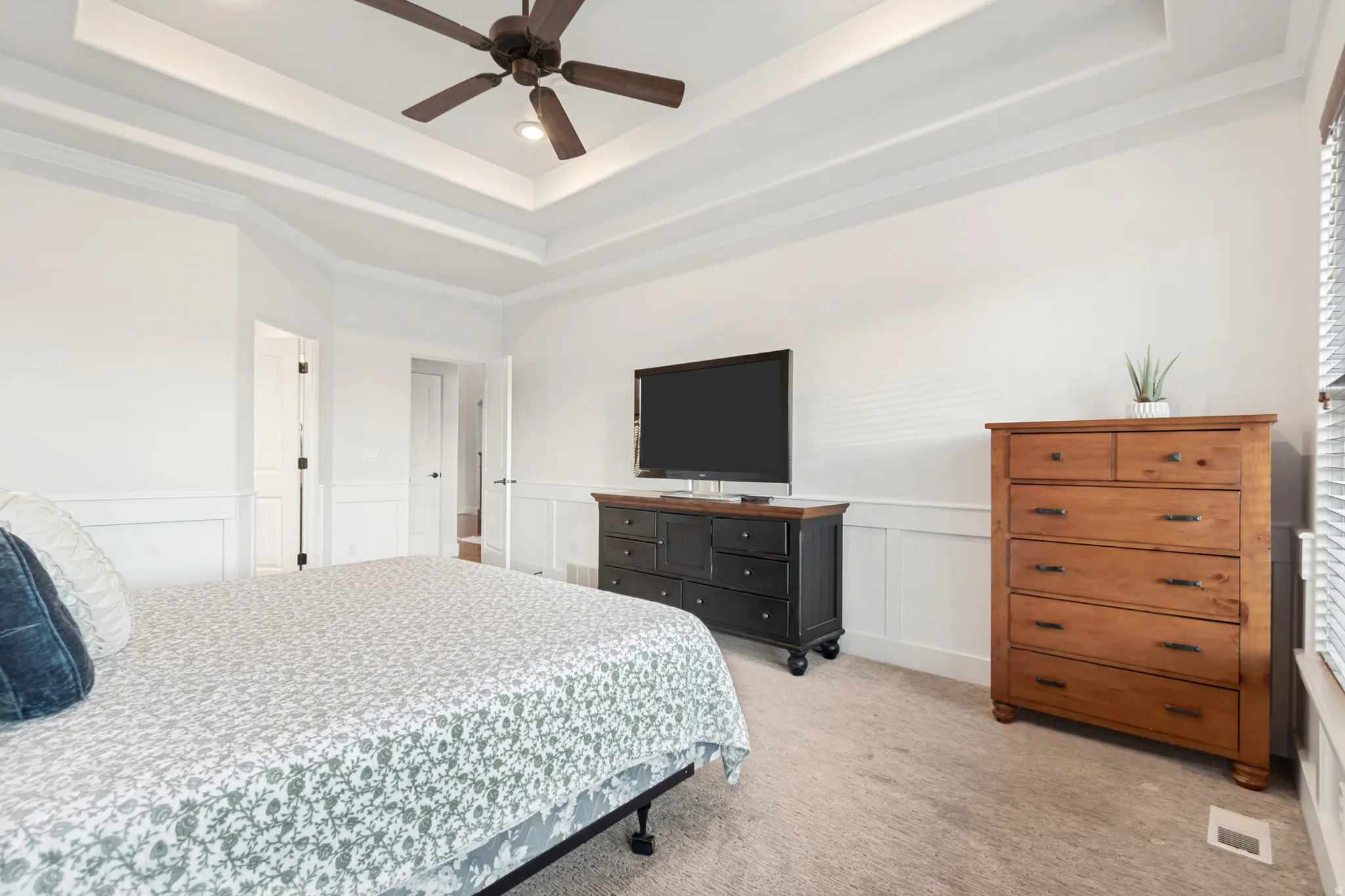 Main floor primary suite bedroom with tray ceiling and ceiling fan.