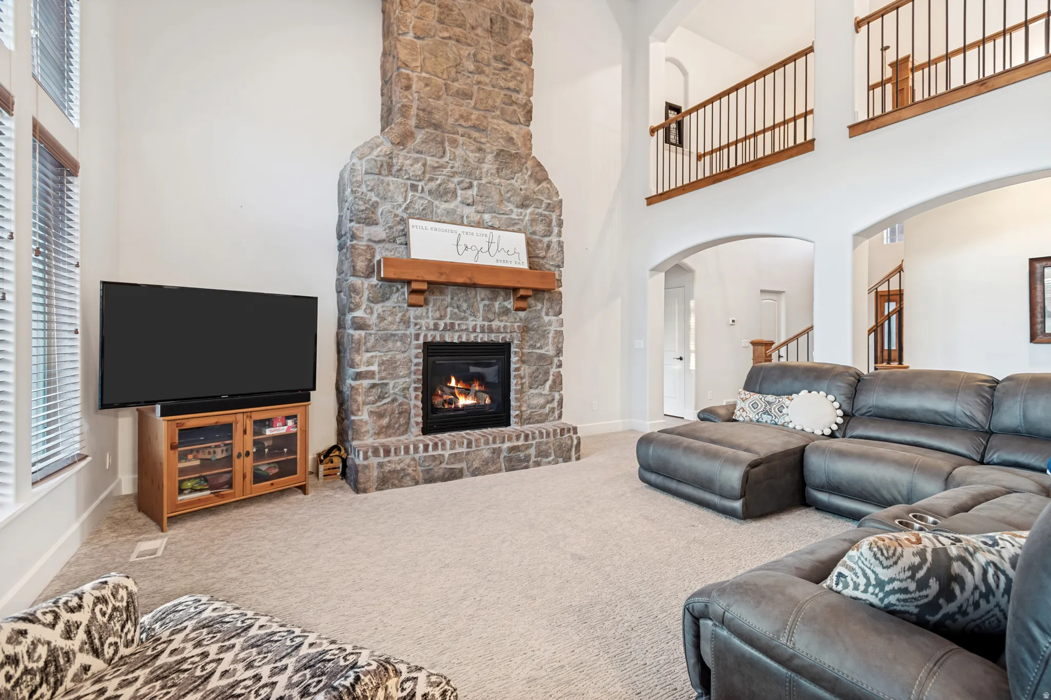 Great room featuring vaulted ceilings, a stone fireplace with a wood mantle, and large windows providing ample amounts of natural light.