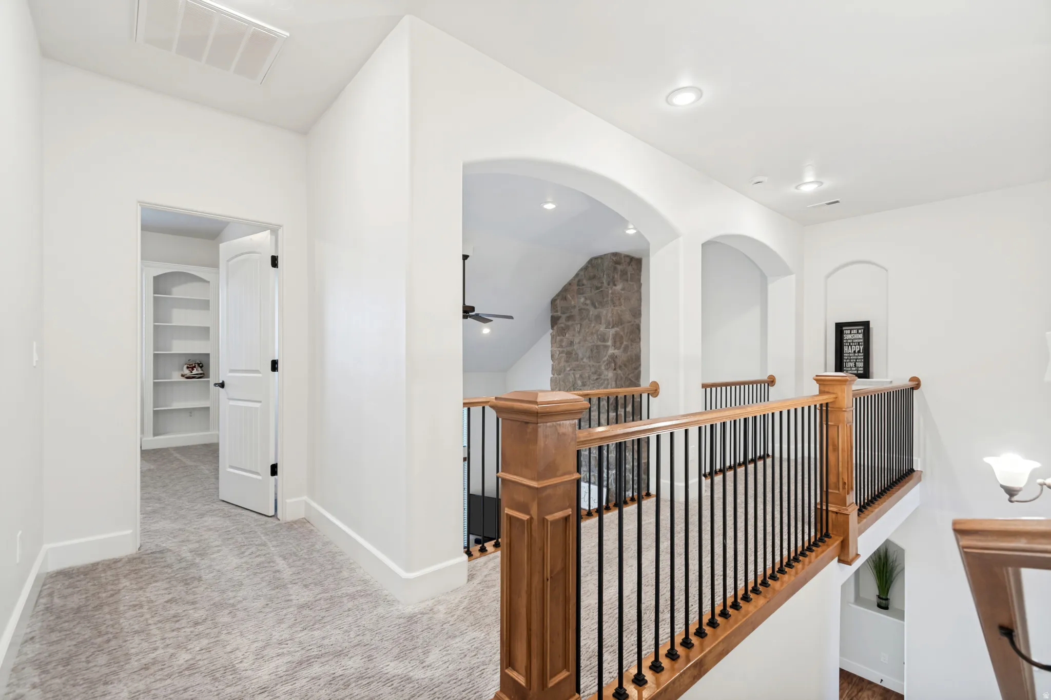 Upper-level landing featuring archway architectural details, recessed lighting, and a wood and wrought iron staircase railing.