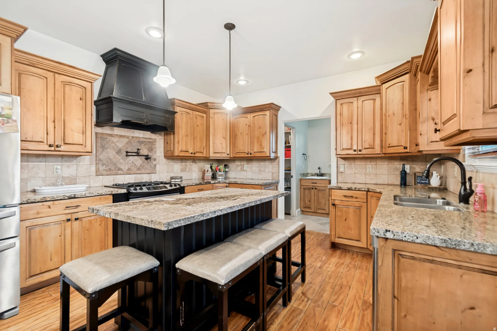 Gourmet kitchen featuring a central island with granite countertop, stainless steel appliances, hardwood flooring, and natural wood cabinetry.