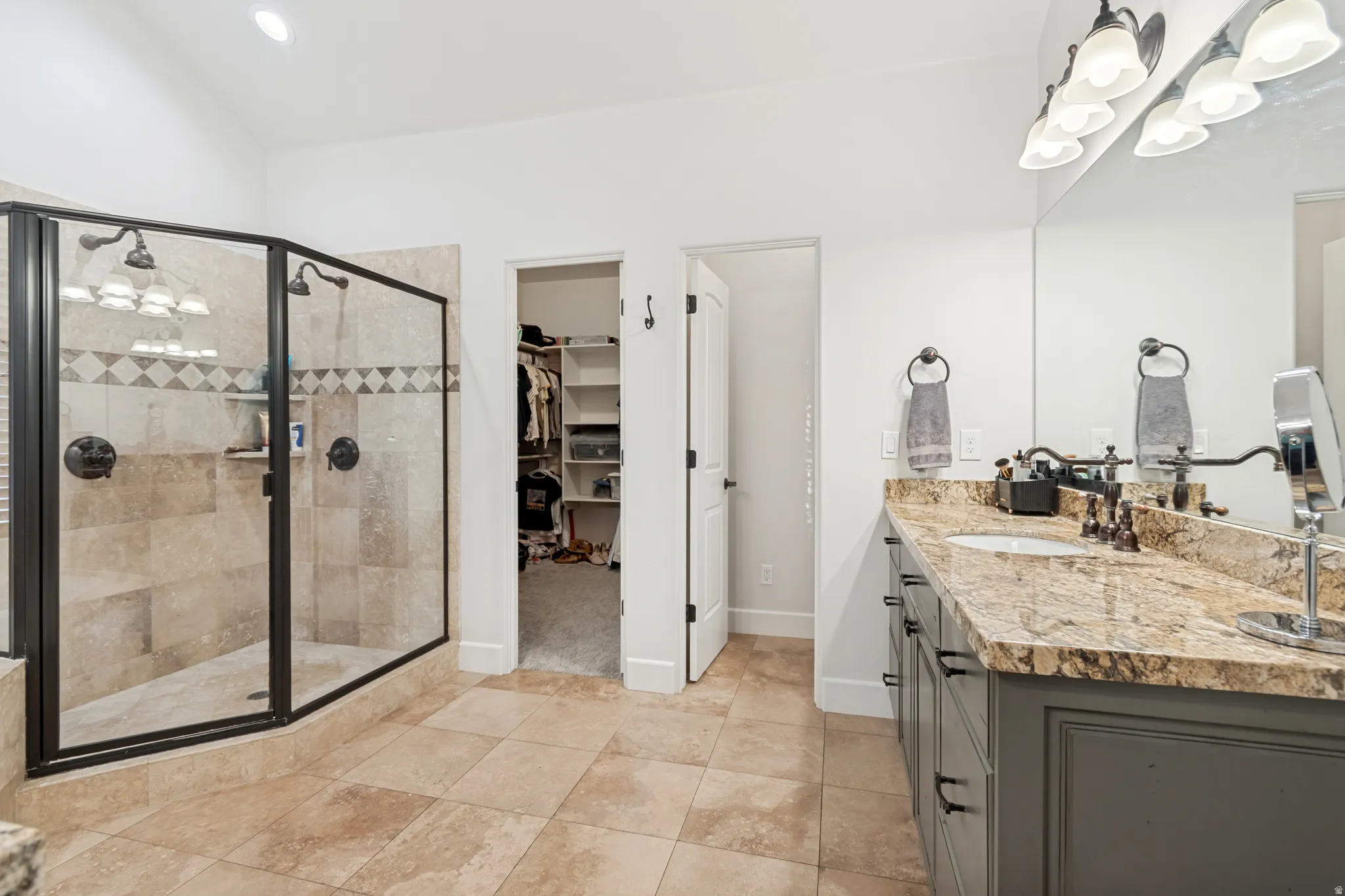 Spacious primary suite bathroom featuring a vanity with granite countertop, large walk-in shower with tile surround, and dual shower heads, and walk-in closet.