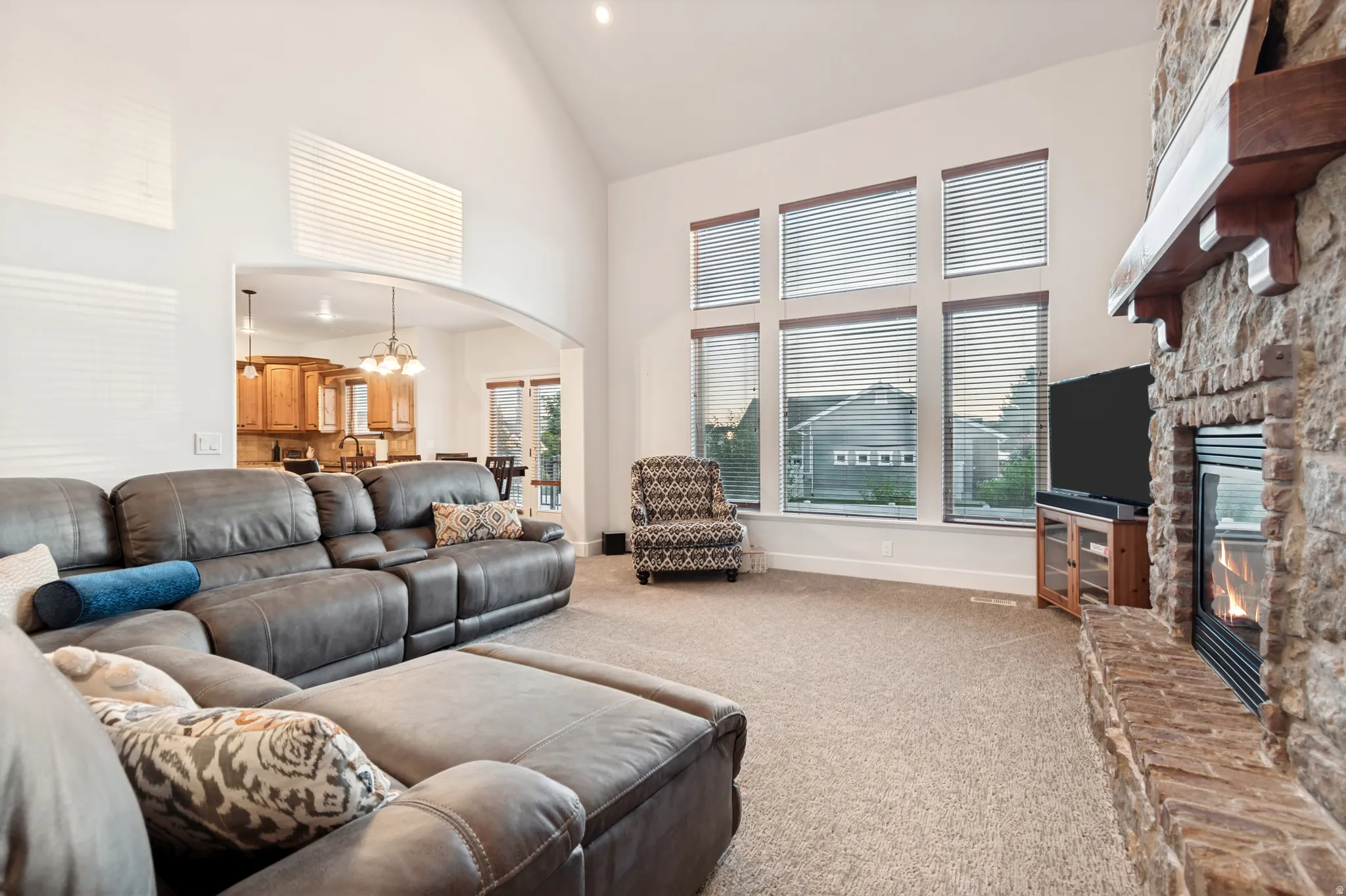 Great room featuring vaulted ceilings, a stone fireplace with a wood mantle, and large windows providing ample amounts of natural light.