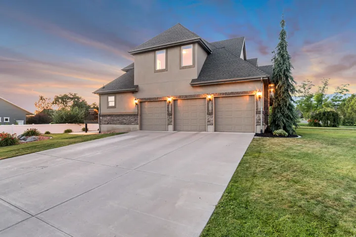 Stucco and stone facade home featuring a three-car garage with individual doors and exterior lighting