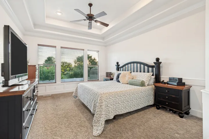 Main floor primary suite bedroom with tray ceiling and ceiling fan.