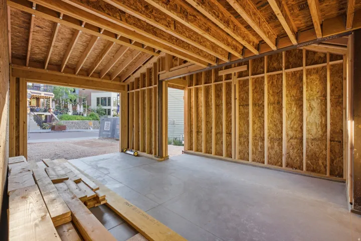 Unfinished garage space featuring exposed wood framing, concrete flooring, and an open entryway to the exterior