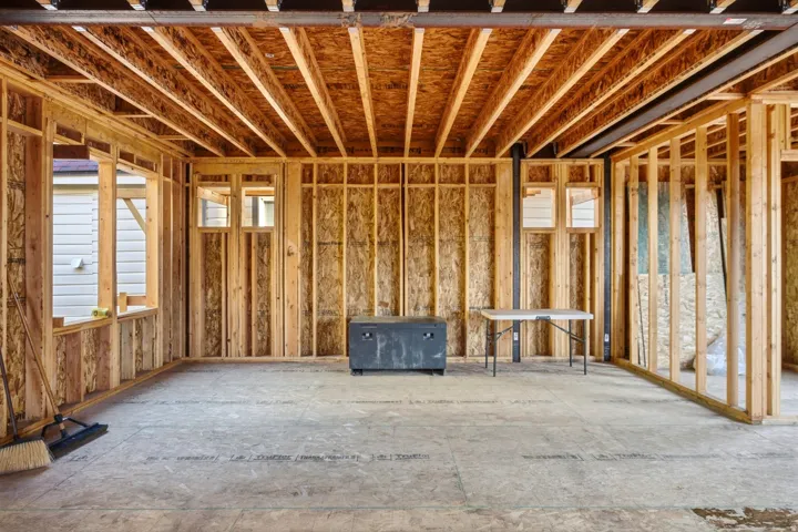 Unfinished interior framing with exposed wood joists and subflooring, featuring multiple window openings