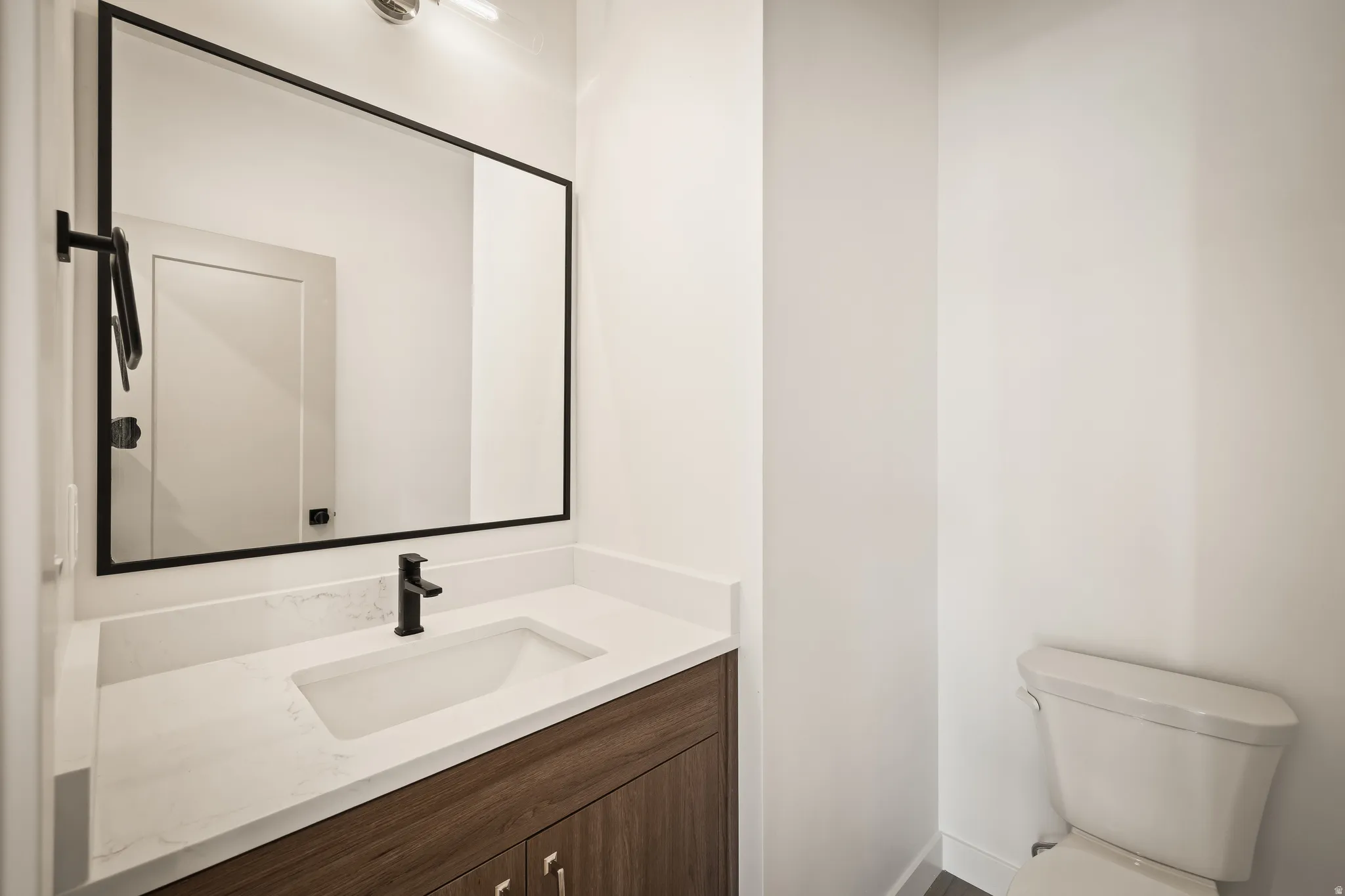 Bathroom featuring a wood-finish vanity with a white quartz countertop, undermount sink, and matte black faucet
