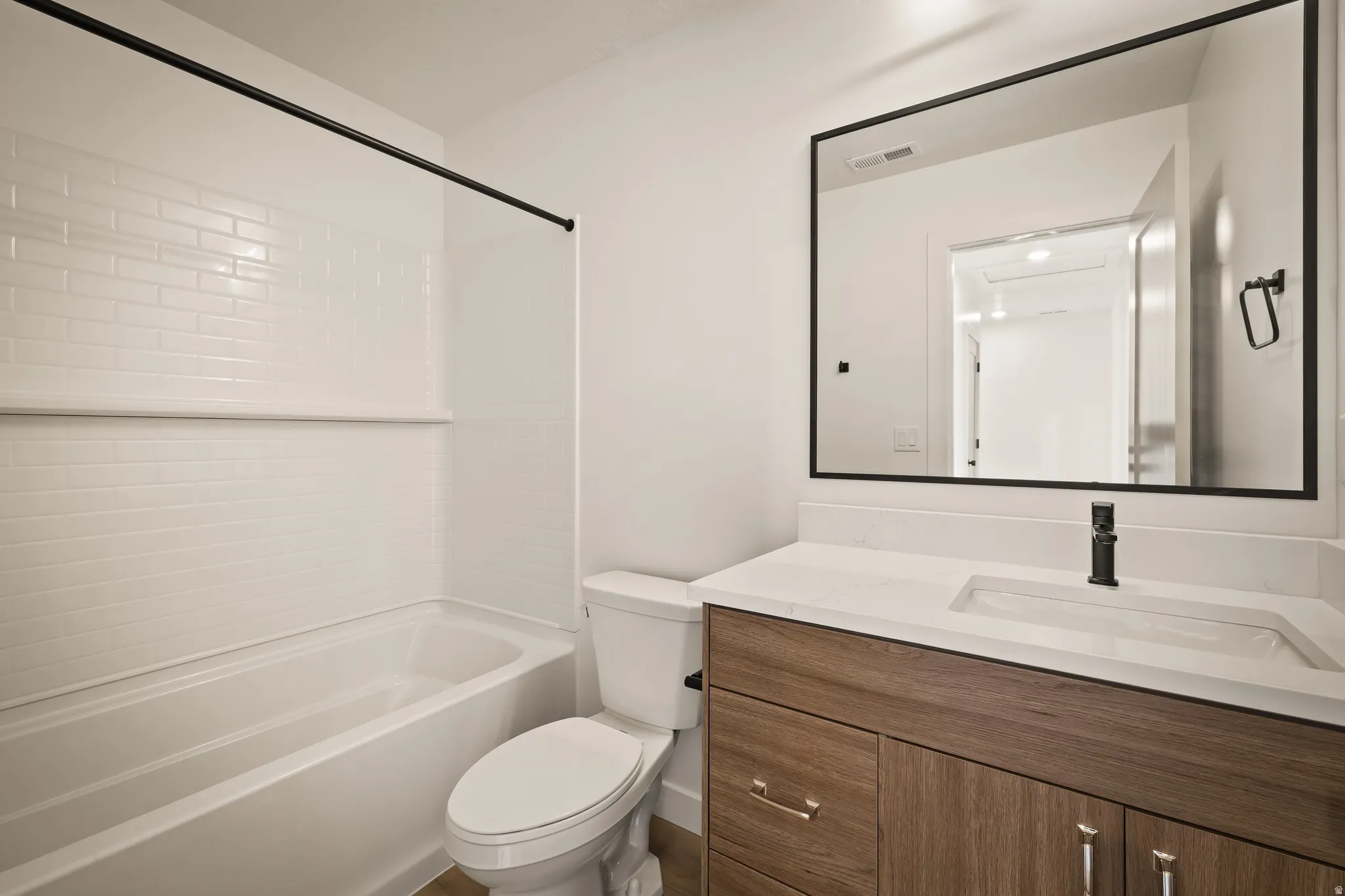 Bathroom featuring a white subway tile surround, integrated bathtub, wood-finish vanity with a single basin sink, and a framed mirror
