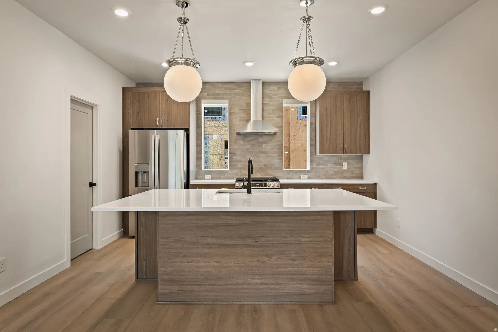 Modern kitchen featuring a central island with a white countertop, wood-finish cabinetry, stainless steel appliances, a tile backsplash, and recessed lighting