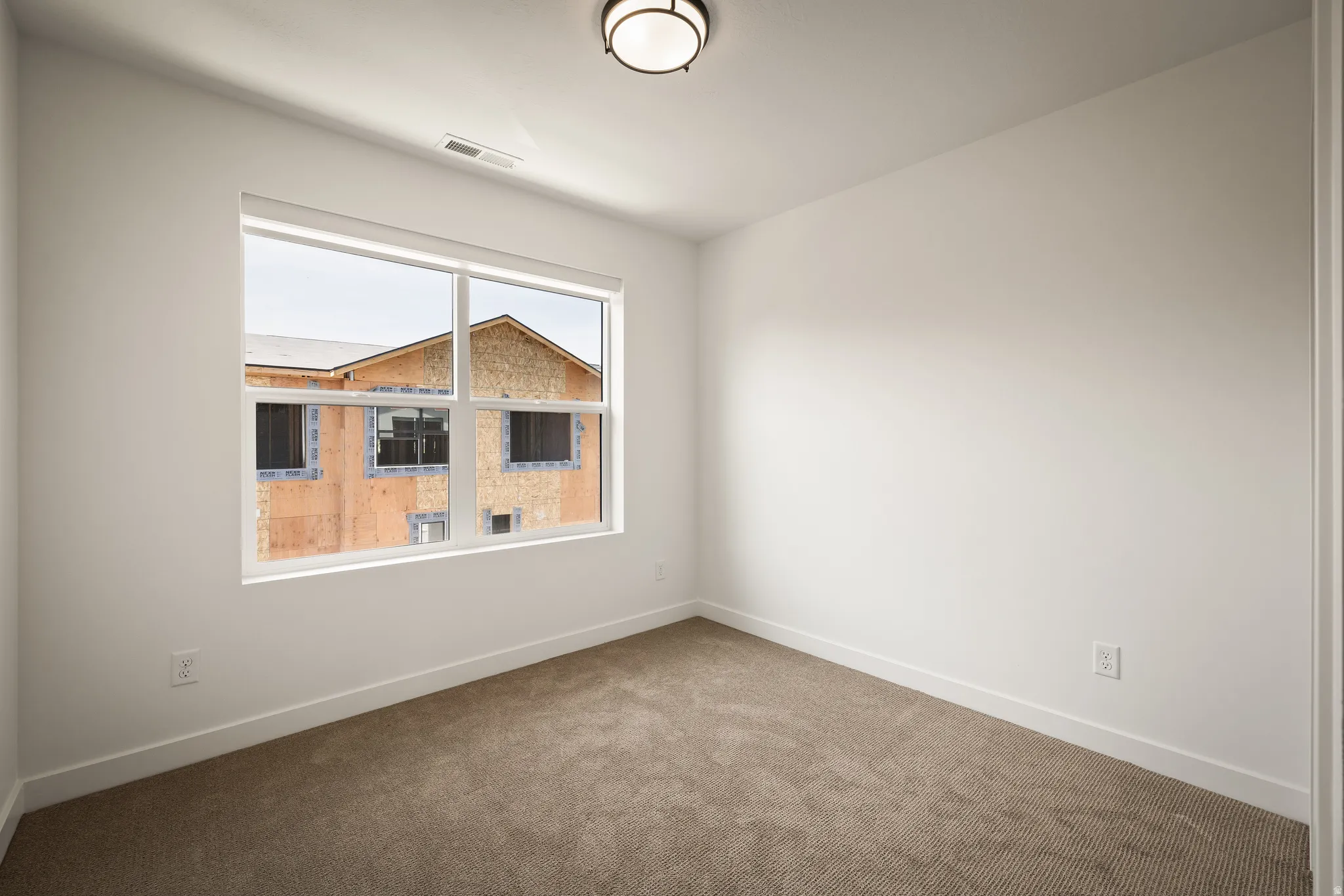 Bright room featuring a large window, neutral carpet flooring, white walls, and a ceiling-mounted light fixture