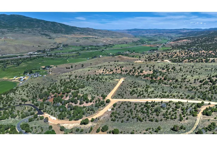 Expansive undeveloped land featuring natural foliage and a dirt road, offering a mountain and valley backdrop