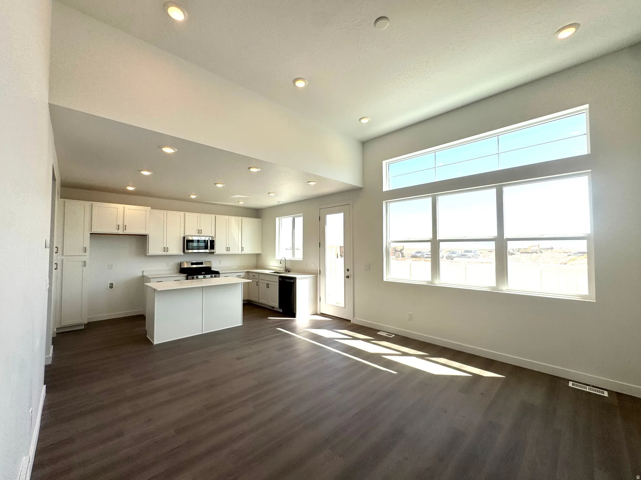Open-concept living area featuring a modern kitchen with white cabinetry, stainless steel appliances, and a central island