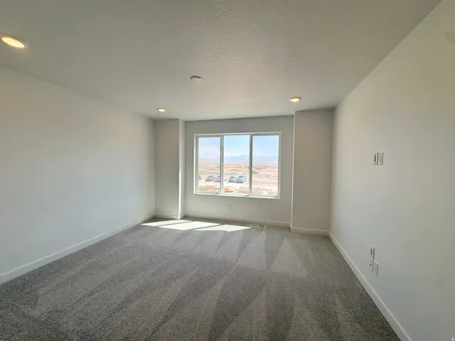 Spacious room featuring a large window, recessed lighting, neutral wall finishes, wide baseboards, and patterned carpeting