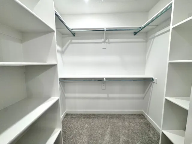 Walk-in closet featuring white built-in shelving, multiple chrome hanging rods, and gray carpet flooring